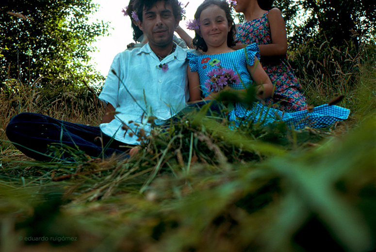 En el monte, un chico y una niña con un manojo de flores silvestres en la mano mirando a cámara.