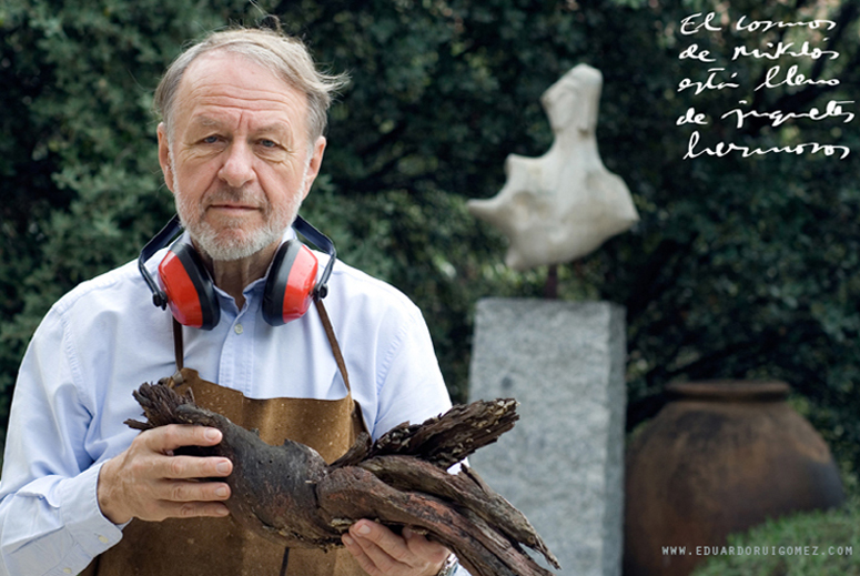 Un escultor mira hacia la cámara. En la mano sostiene una escultura de madera.