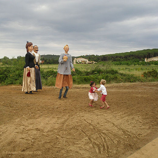 Gigantes y cabezudos observando a dos niños bailando en el campo.