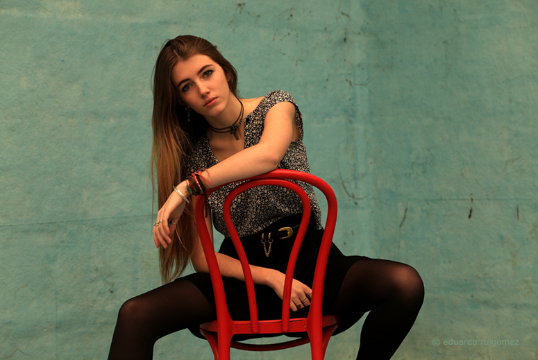 Chica sentada en una silla roja en el fondo de una piscina vacía.